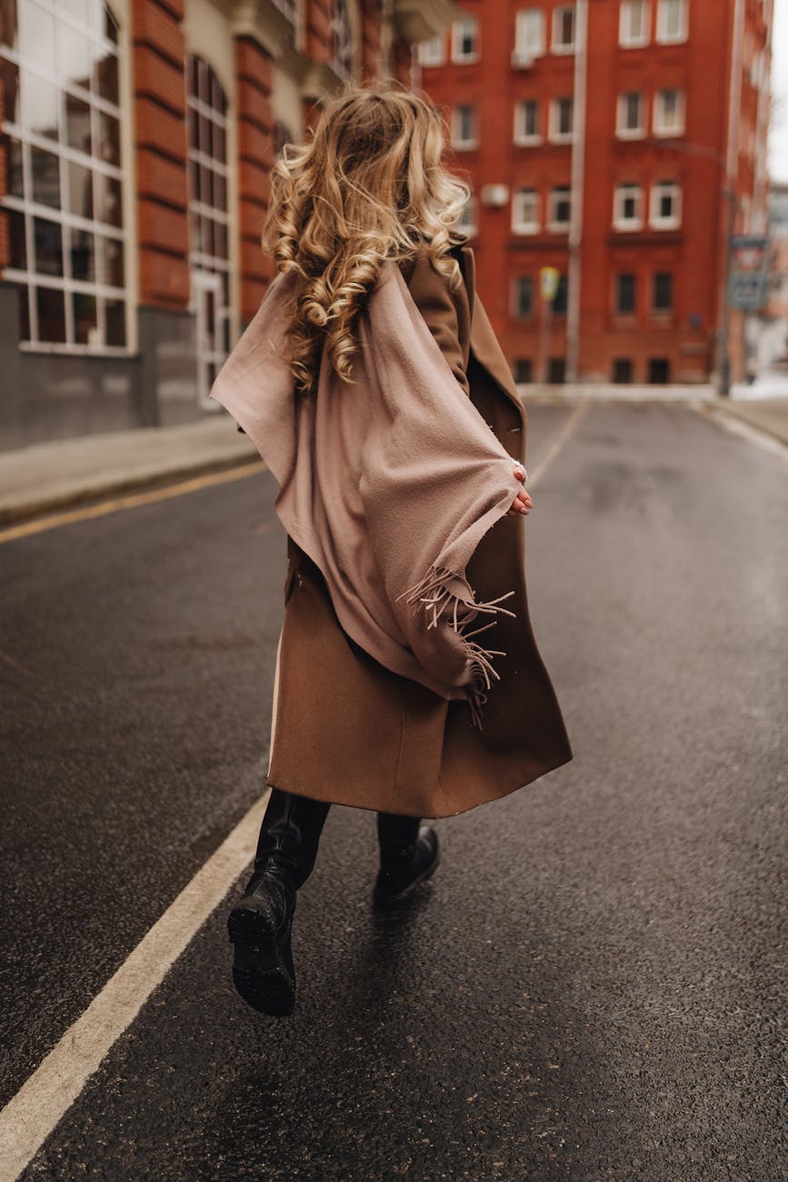 blond woman in winter coat and warm shawl walking in street